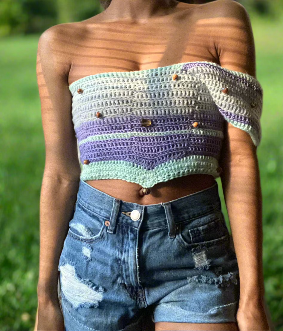 A person wearing a multicolored crochet crop top with long sleeves and a V-neckline, paired with blue denim shorts.