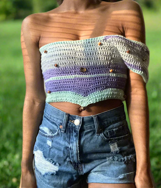 A person wearing a multicolored crochet crop top with long sleeves and a V-neckline, paired with blue denim shorts.