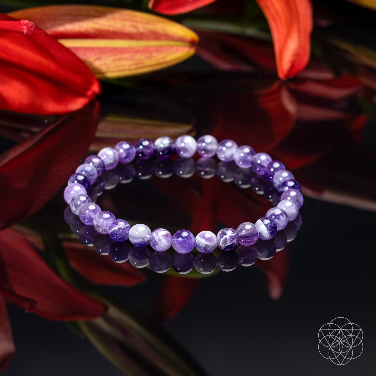 A beaded stretch bracelet made of round purple and white marbled gemstone beads, displayed on a reflective dark surface with red flowers in the background.