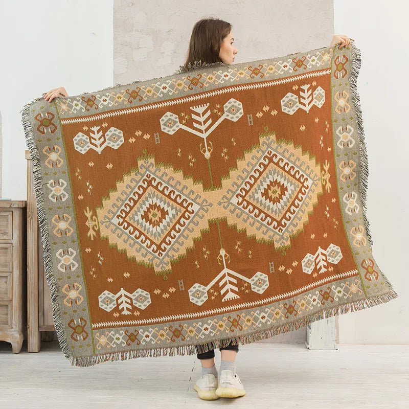 Person holding a large decorative blanket with geometric patterns in a minimalistic room.