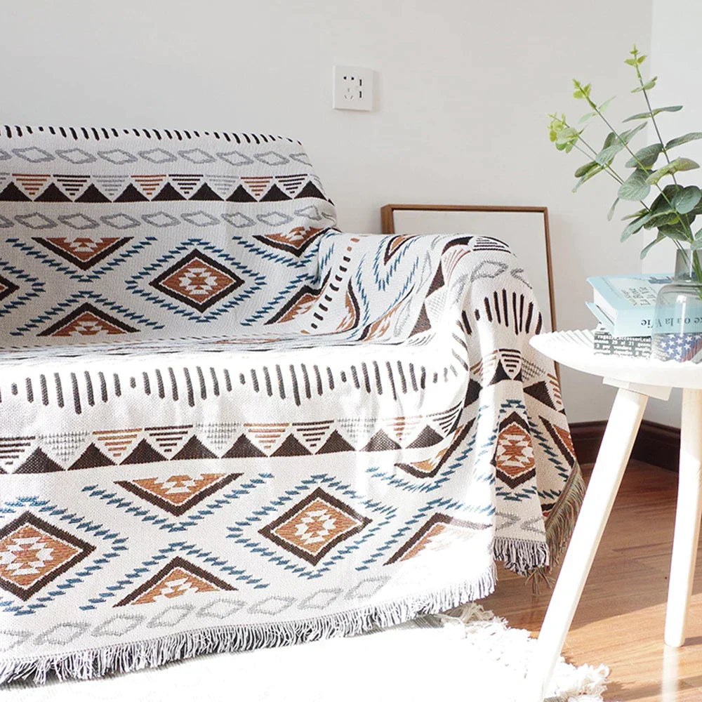 Patterned throw blanket on a sofa with a side table and plant in the background