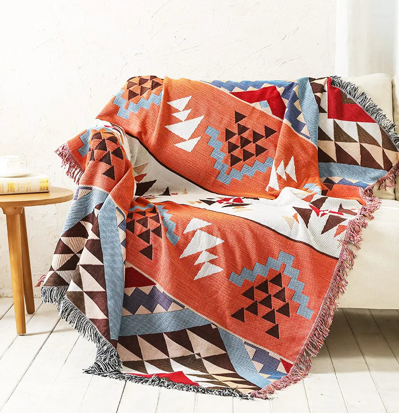 Geometric patterned blanket draped over a sofa in a room with a wooden table.