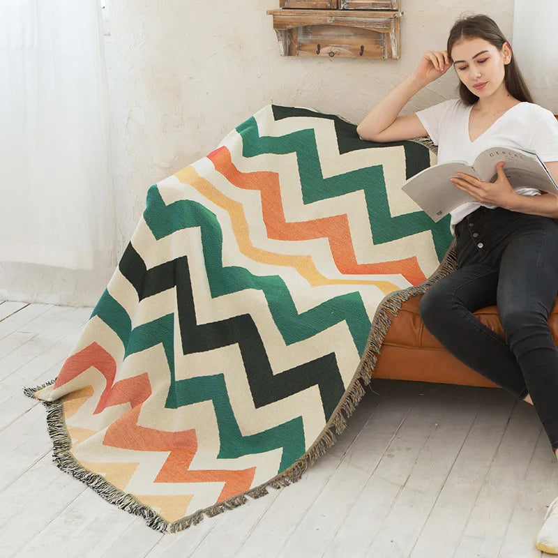 Woman reading a book under a colorful zigzag patterned blanket on a couch.