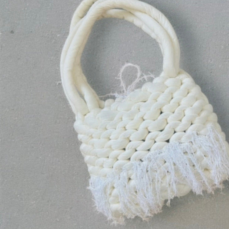 White woven bag with fringes on a gray background