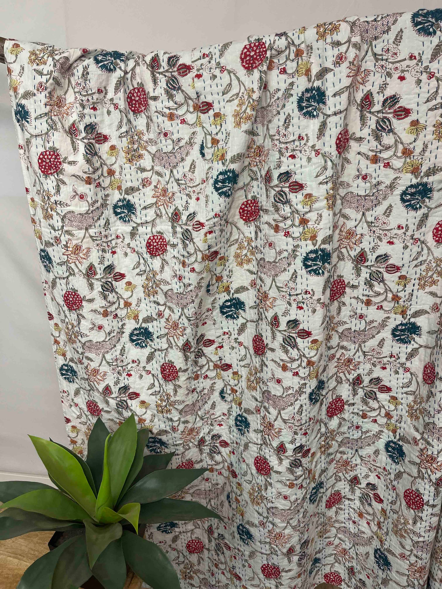 Floral patterned blanket draped over a surface with a plant in the foreground.