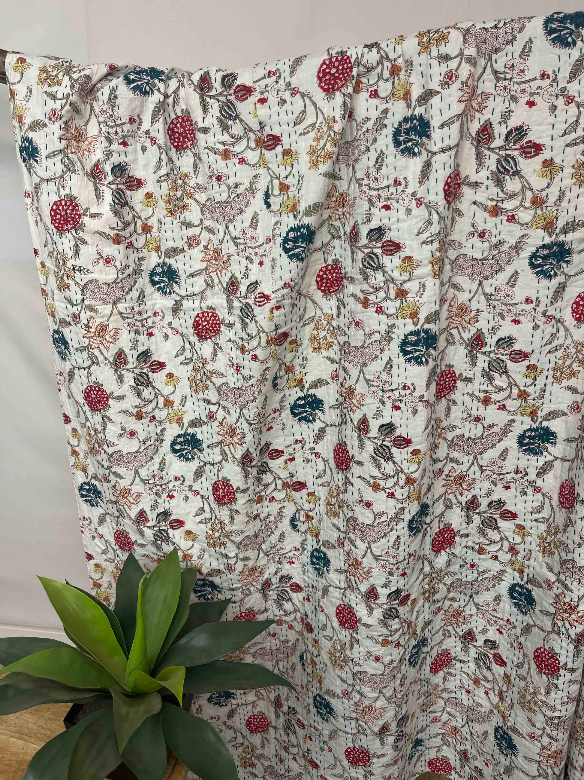 Floral patterned blanket draped over a surface with a plant in the foreground.