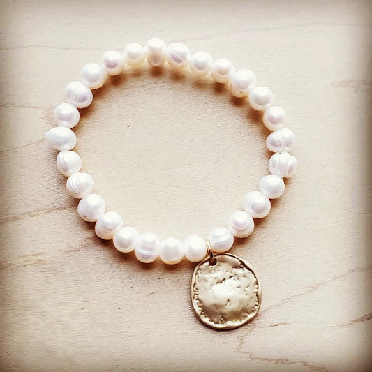 Pearl bracelet with a gold charm on a light wooden surface