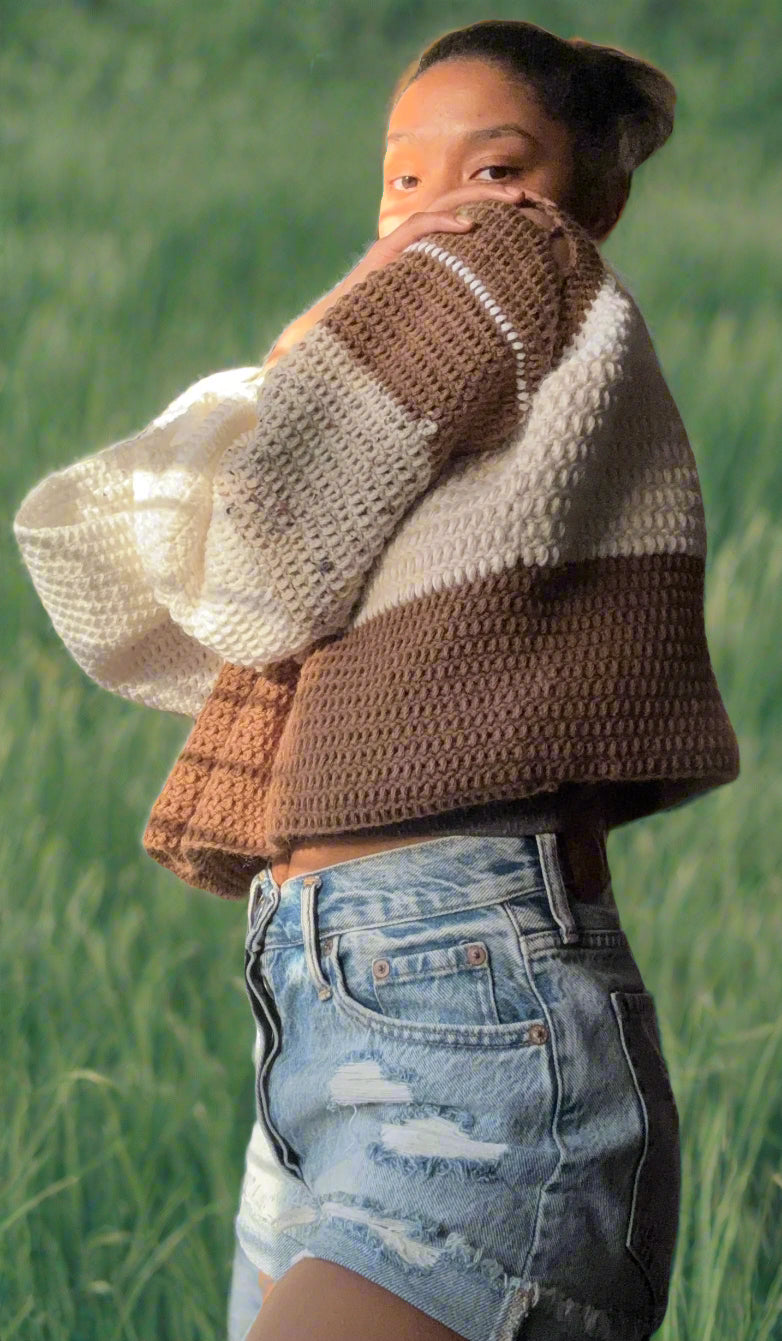 girl wearing a color-block sweater. the neckline begins with white, then turns to beige, then brown on the body of the sweater. The sleeves descend from brown to beige to white. 
