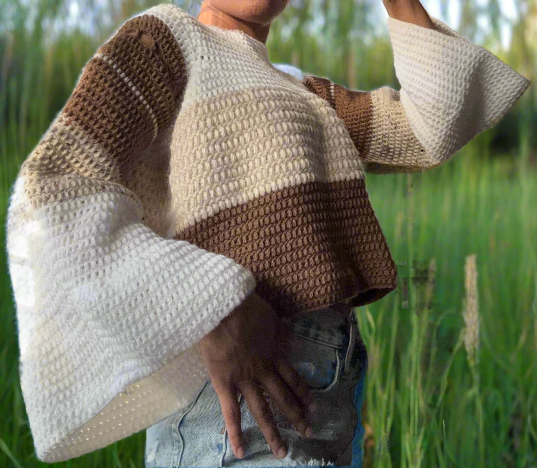 girl wearing a color-block sweater. the neckline begins with white, then turns to beige, then brown on the body of the sweater. The sleeves descend from brown to beige to white. 