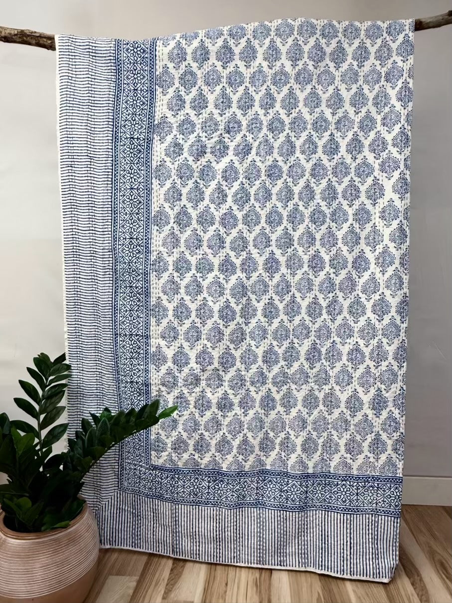 Blue and white patterned throw blanket on a wooden surface with a plant in the background