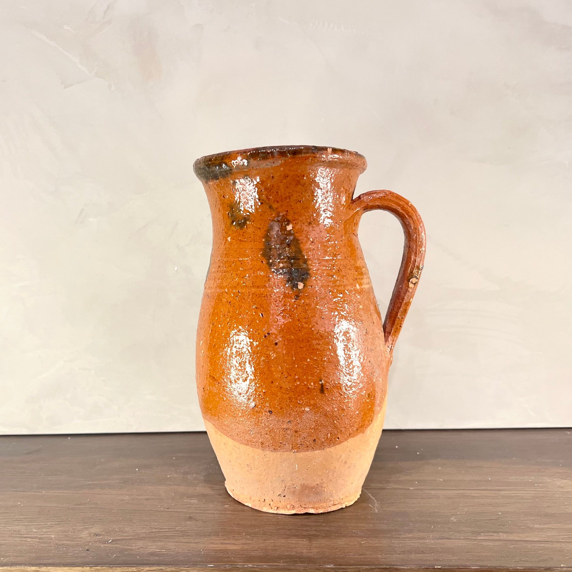 Brown ceramic pitcher on a wooden surface with a white background
