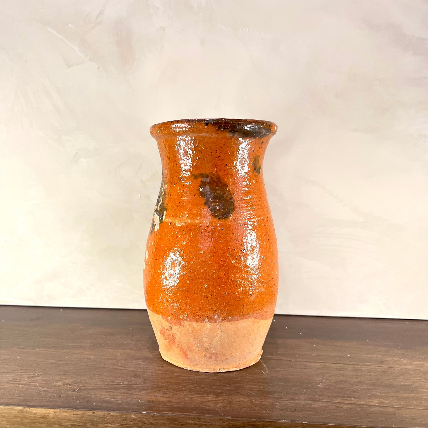 Orange ceramic vase with brown accents on a wooden surface and white background