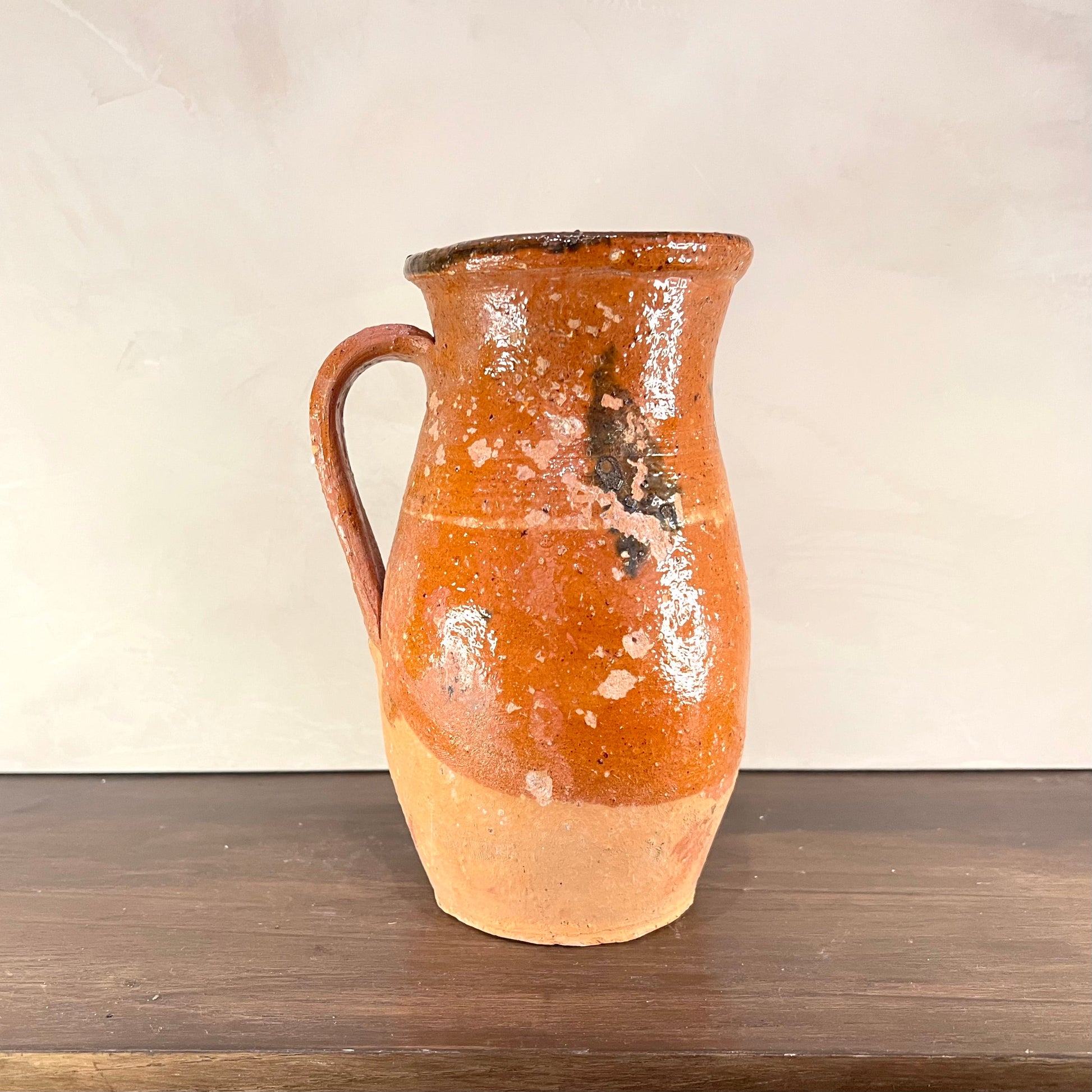 Terracotta pitcher on a wooden surface with a plain background