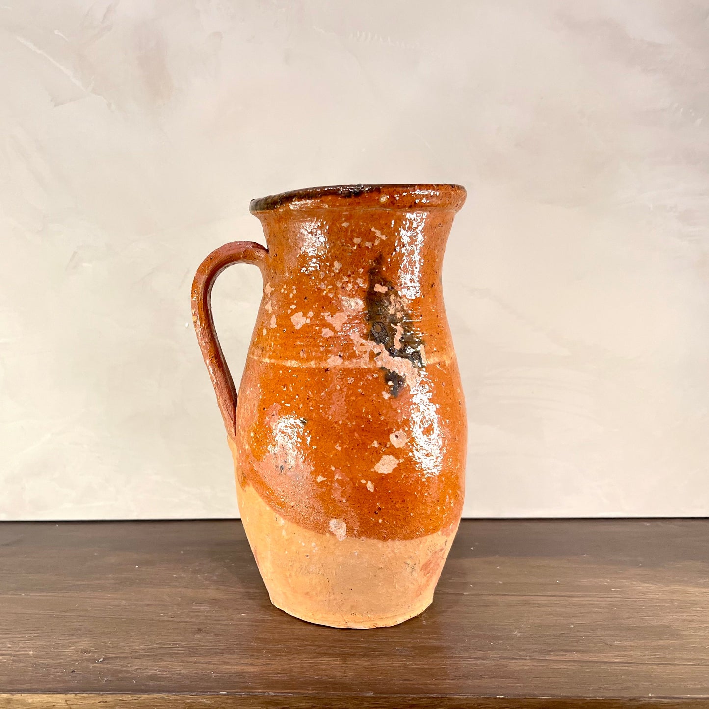 Ceramic pitcher with orange glaze on a wooden surface and beige background