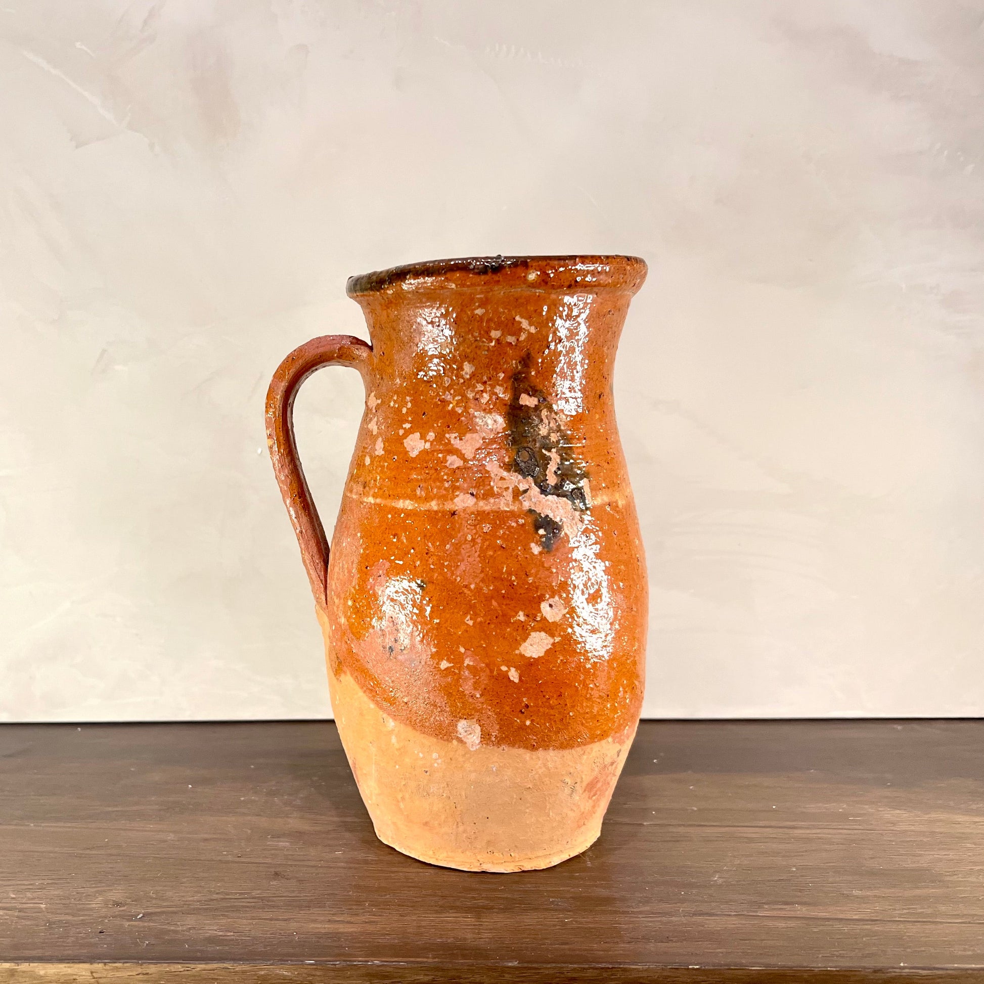 Ceramic pitcher with orange glaze on a wooden surface and beige background