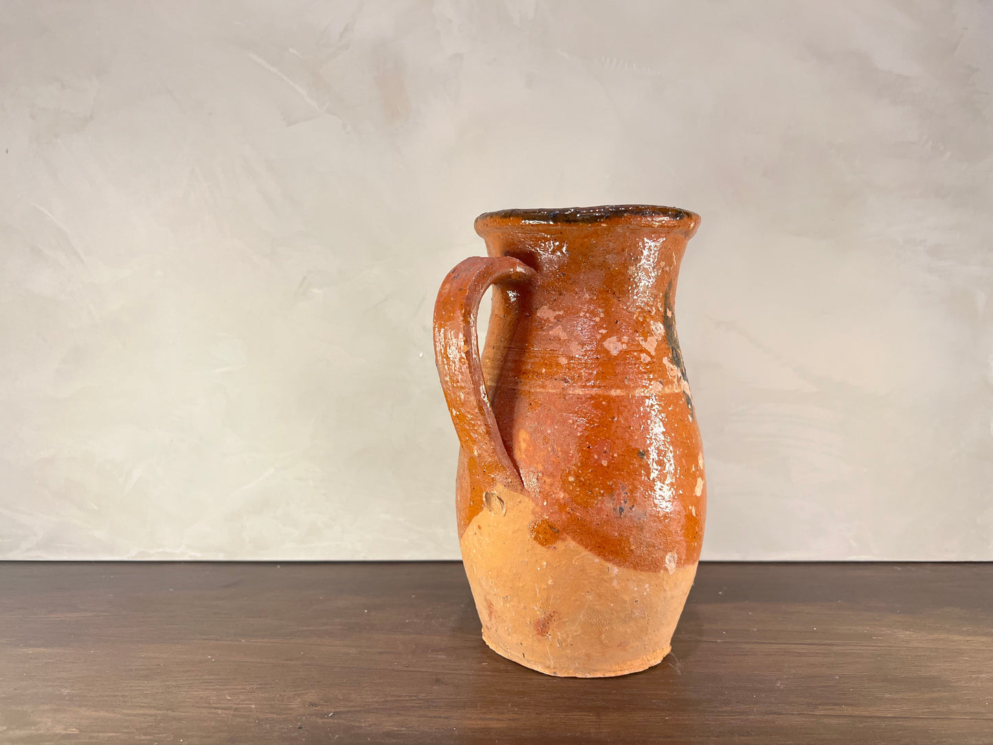 Terracotta pitcher on a wooden surface with a plain background