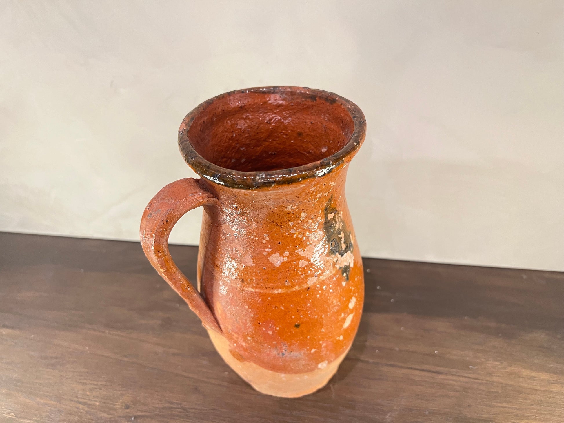 Terracotta pitcher on a wooden surface with a plain background