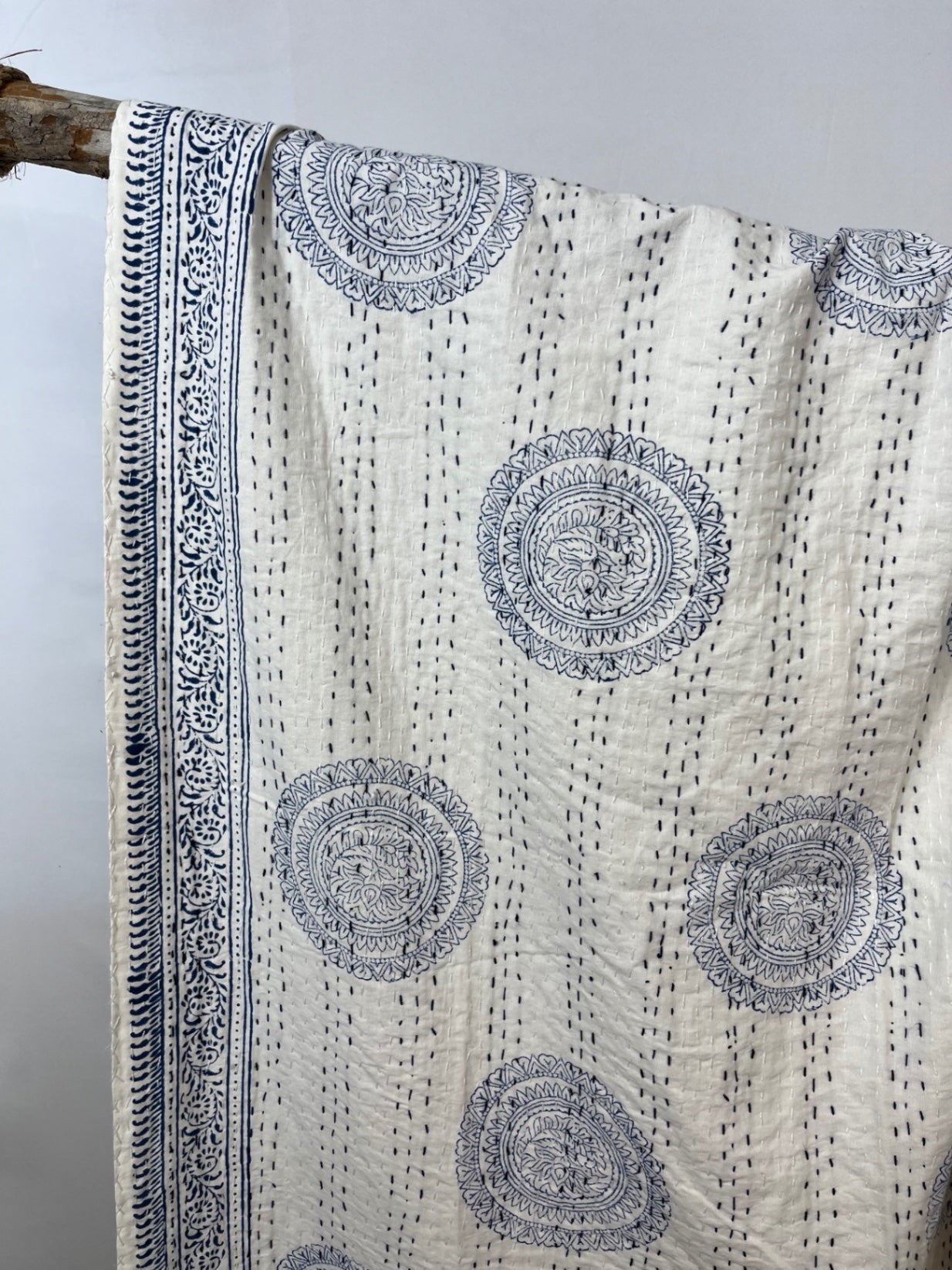 White fabric with black circular patterns and intricate border, draped over a branch.