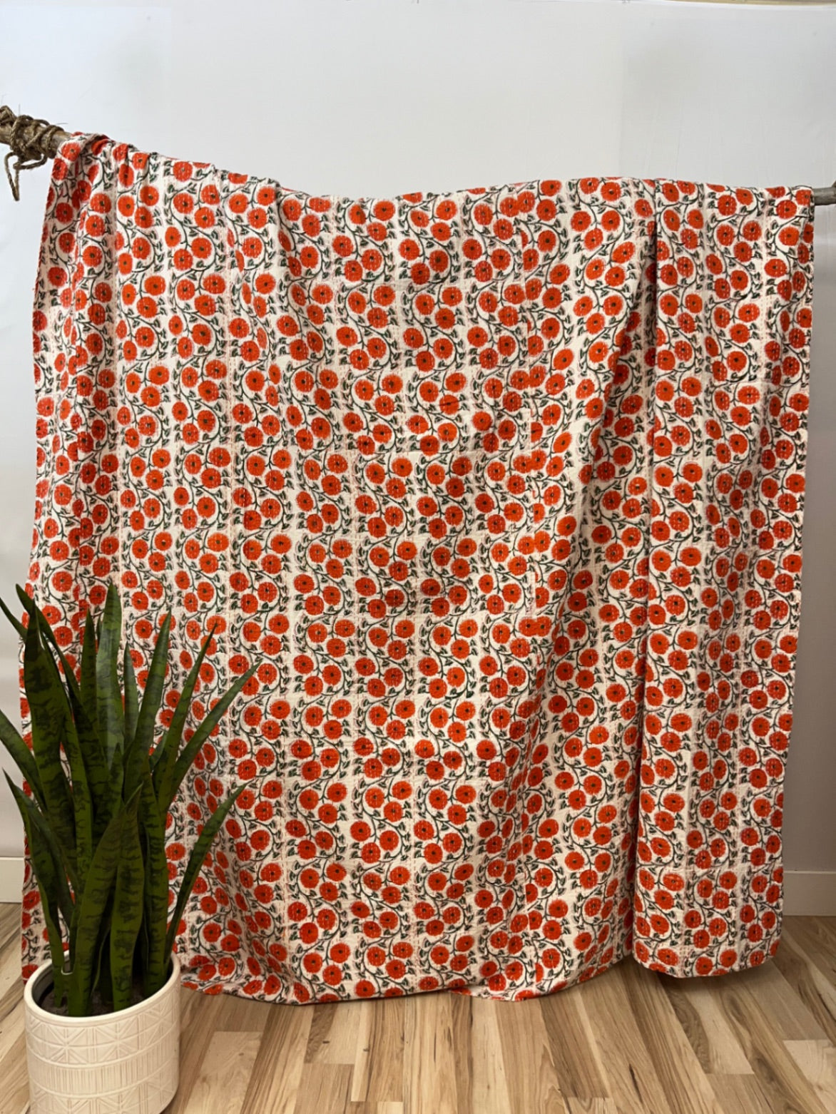 Floral patterned curtain with red flowers on a wooden rod against a white wall.