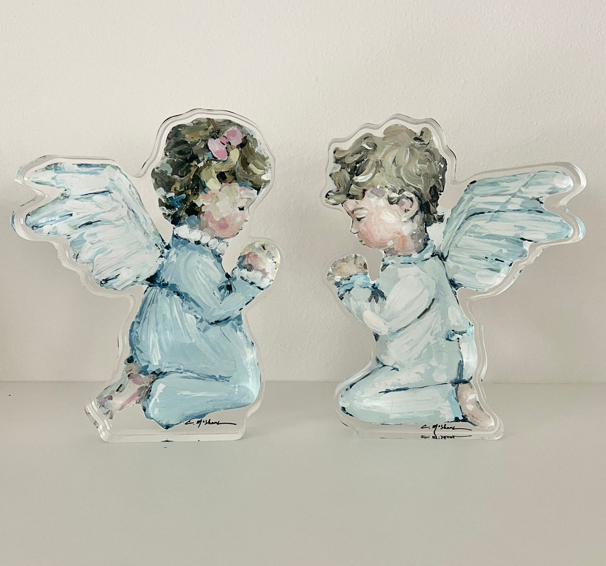 Two angel figurines with blue outfits and white wings on a light gray background