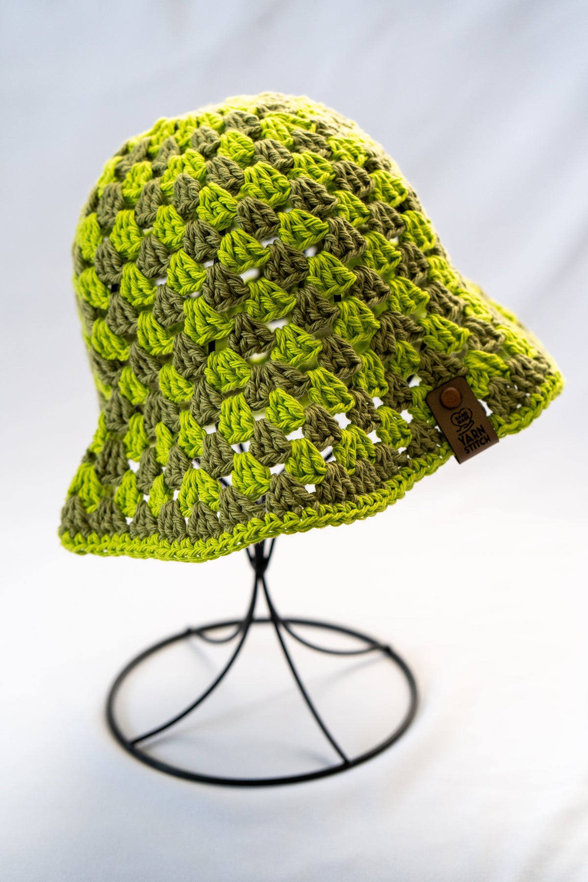 Green crochet hat on a black stand against a light gray background