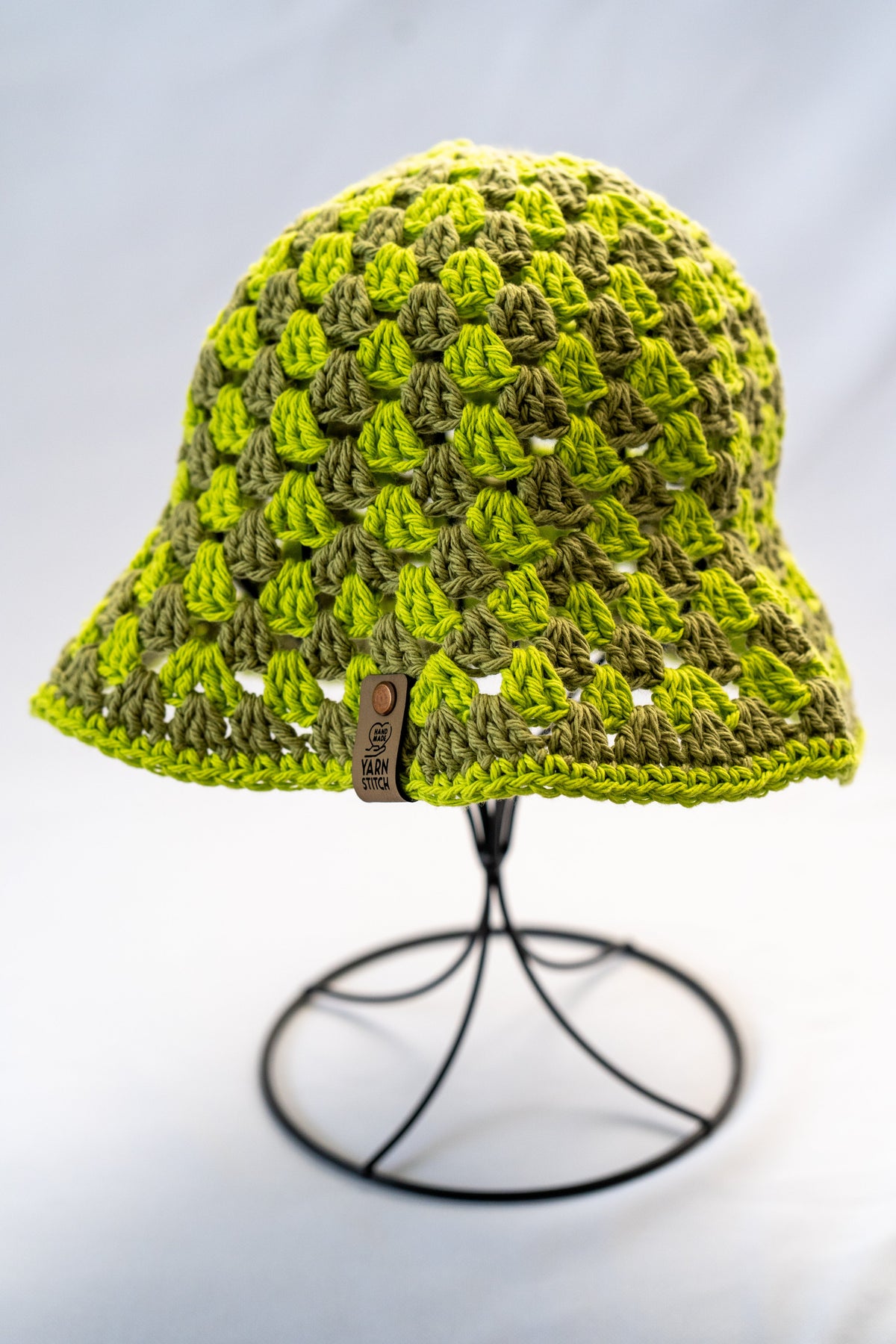 Green crochet hat on a stand against a light gray background