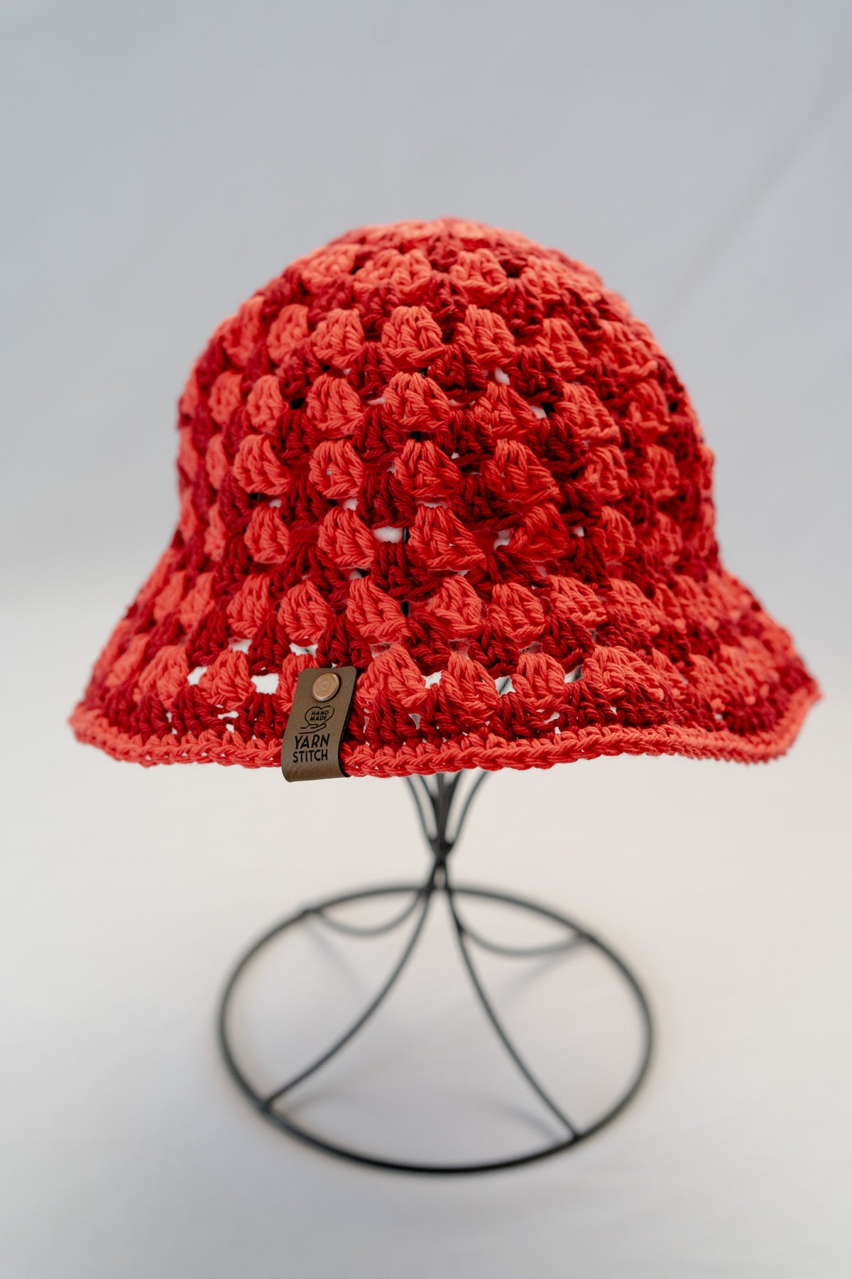 Red crochet hat on a stand against a gray background