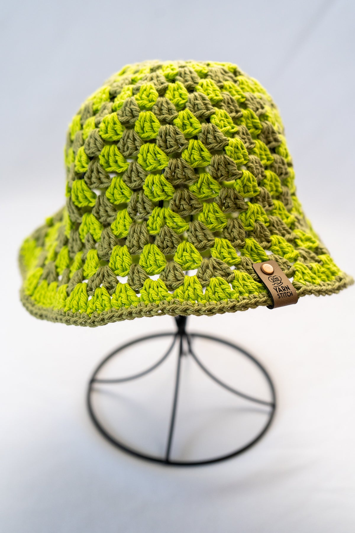 Green crochet bucket hat on a stand with a light gray background
