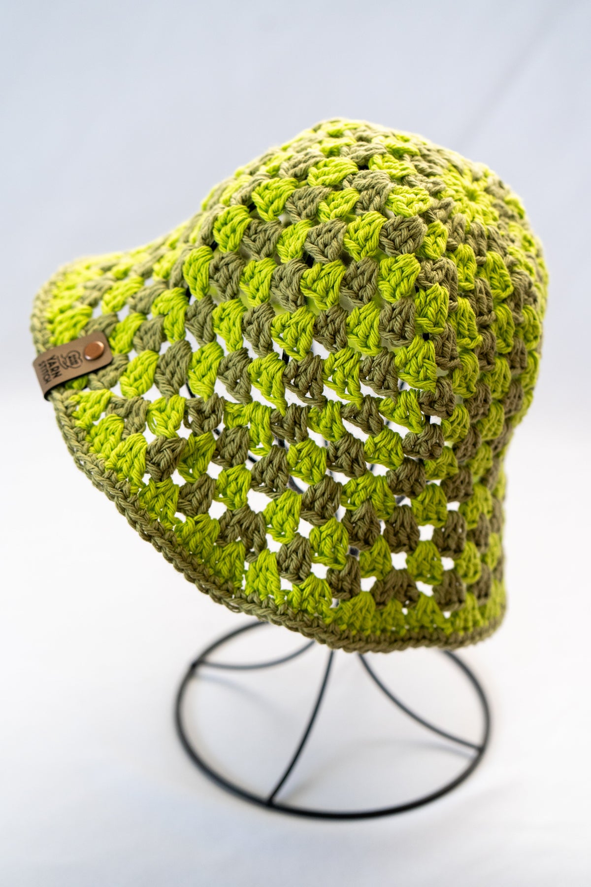 Green crochet hat on a stand against a white background