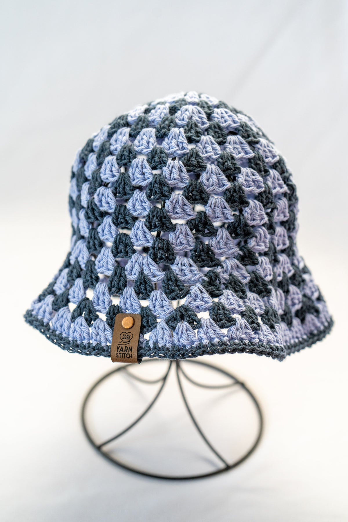 Crocheted bucket hat with a textured pattern on a stand against a white background
