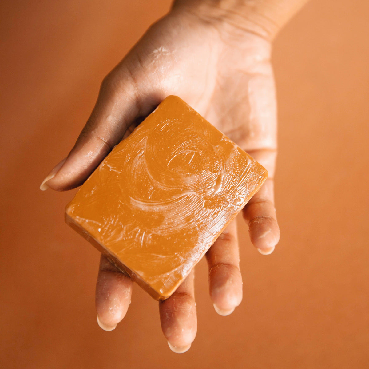 Hand holding a bar of soap against an orange background