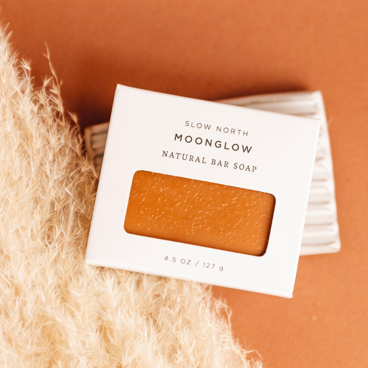 Bar of soap with packaging labeled 'Slow North Moonglow Natural Bar Soap' on a textured surface.