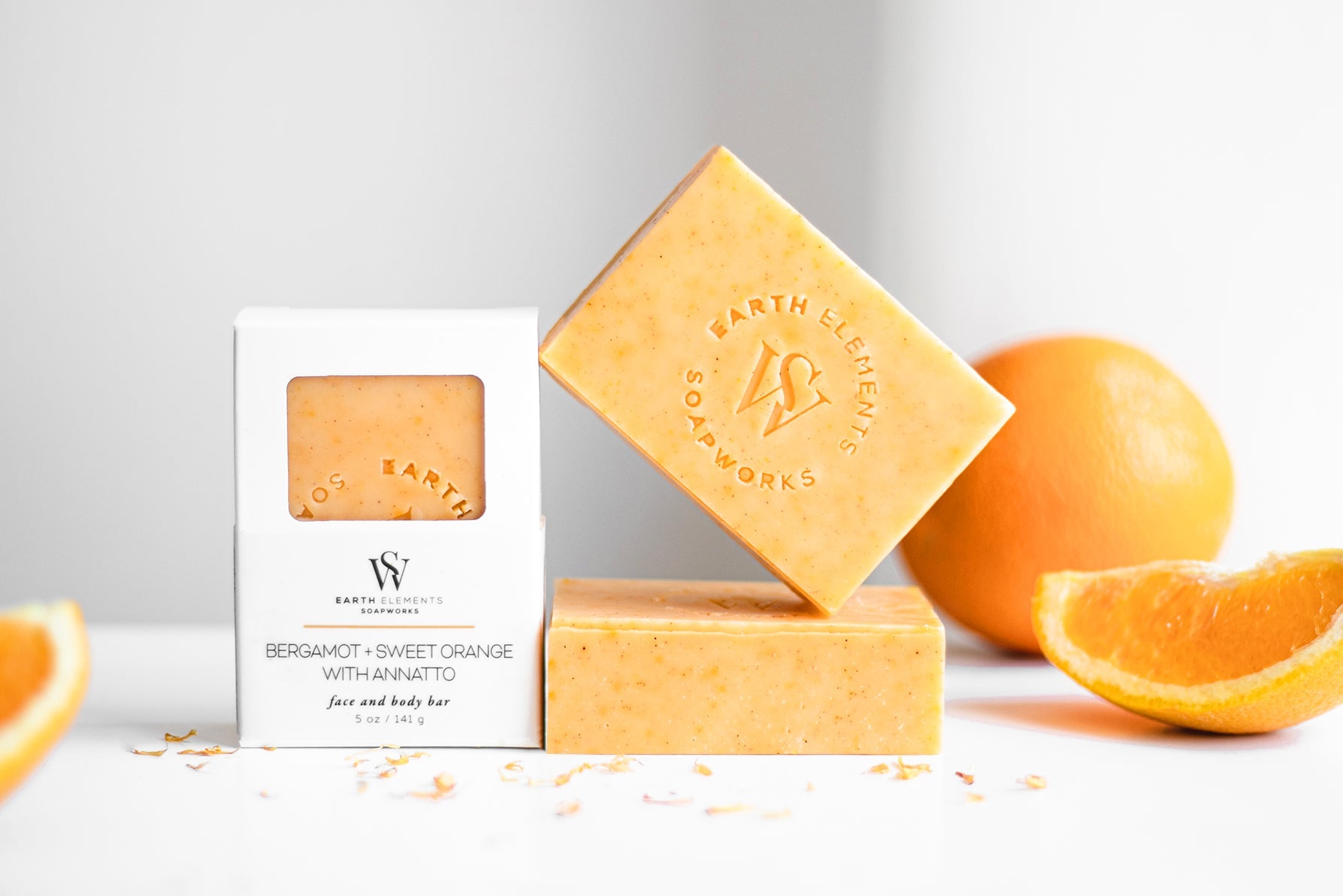 Two bars of soap with a box labeled 'Earthly Bath' and oranges on a light background