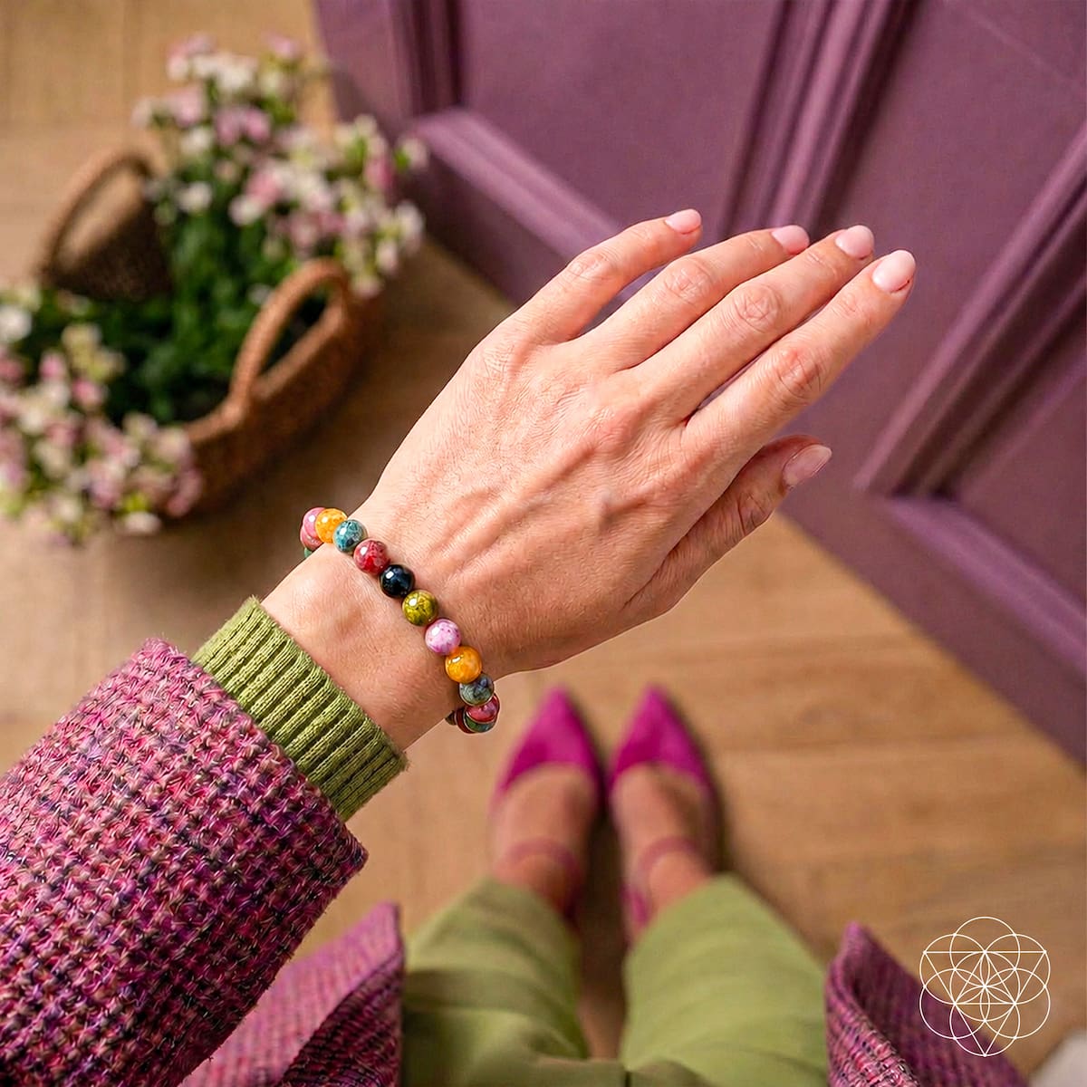 Person wearing a colorful beaded bracelet on a wooden floor with flowers and a purple chair in the background.