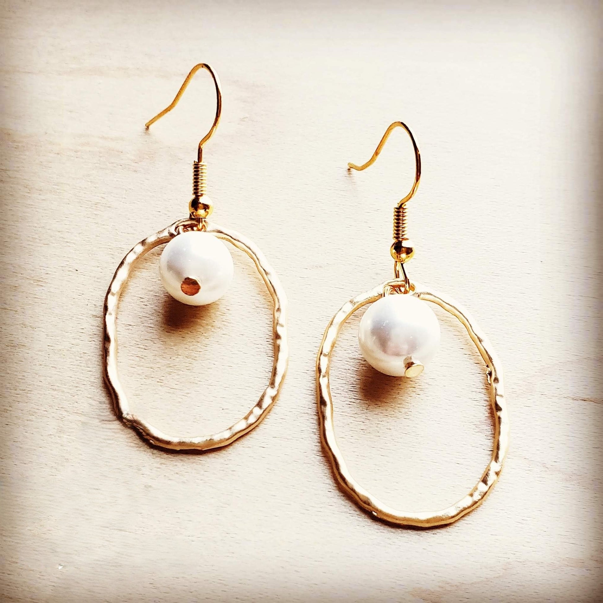 Gold hoop earrings with white pearls on a beige background
