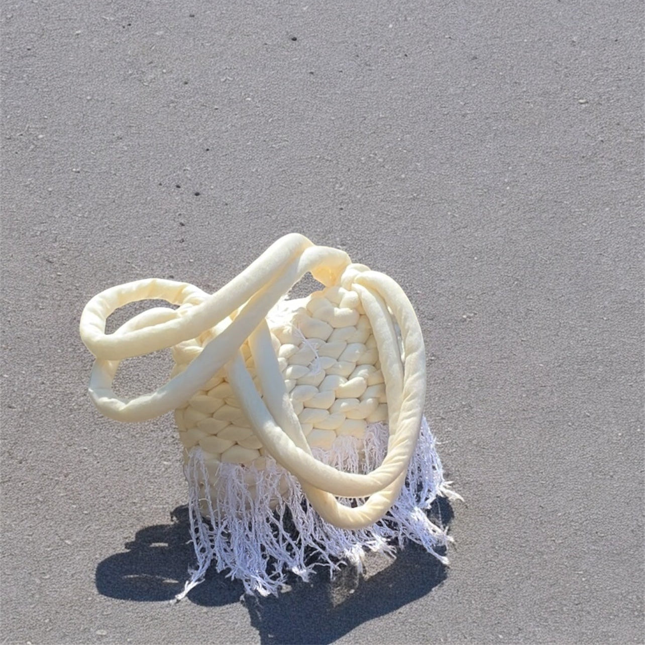White woven bag with fringes on a gray surface
