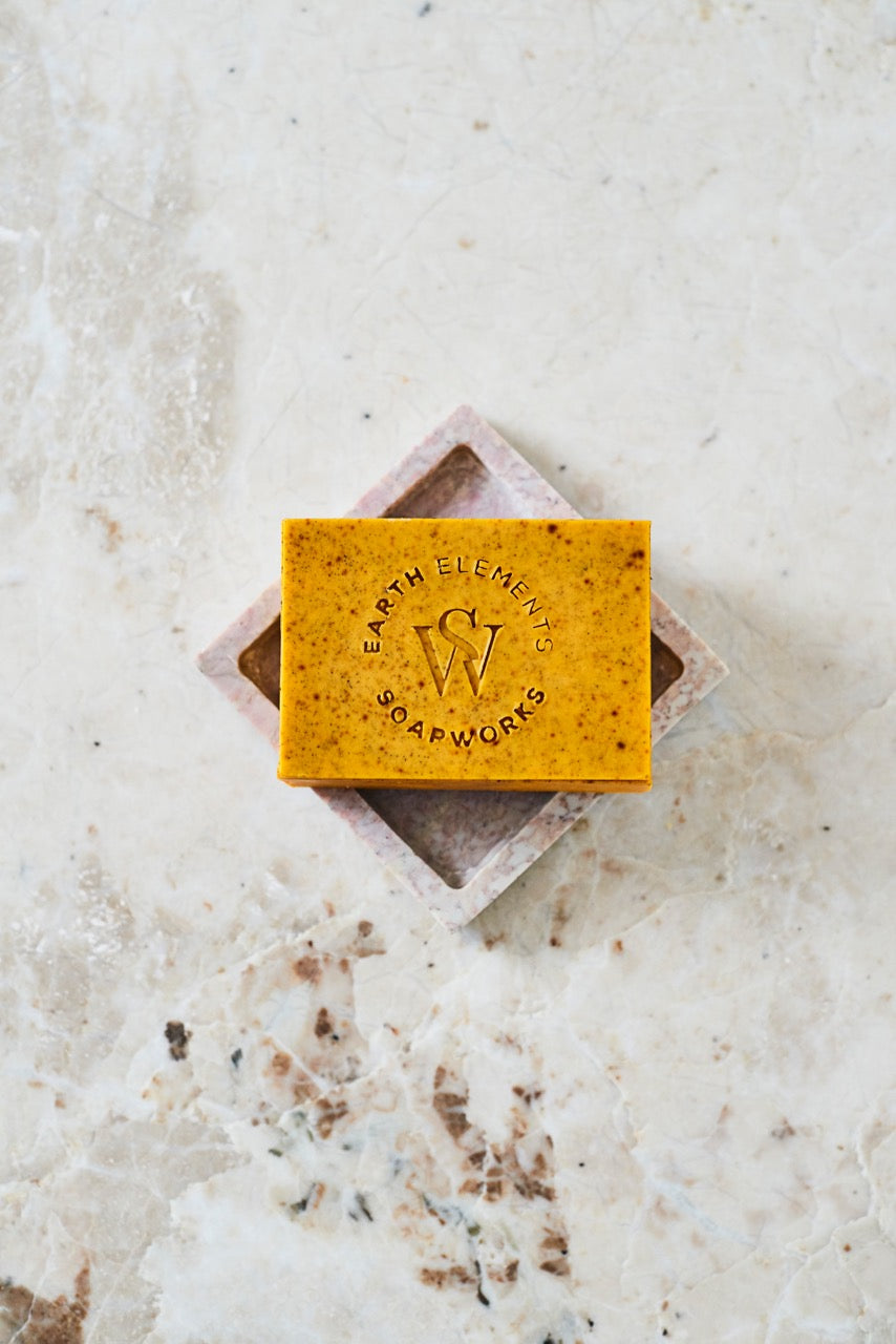 Yellow soap bar with 'Earth Elements Soapworks' branding on a textured white surface