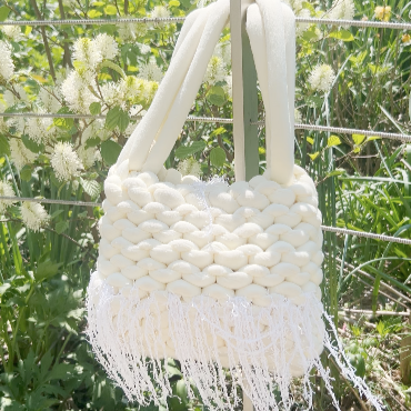 White woven handbag with fringe details against a natural background