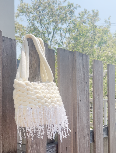 White textured bag with fringes hanging on a wooden fence outdoors