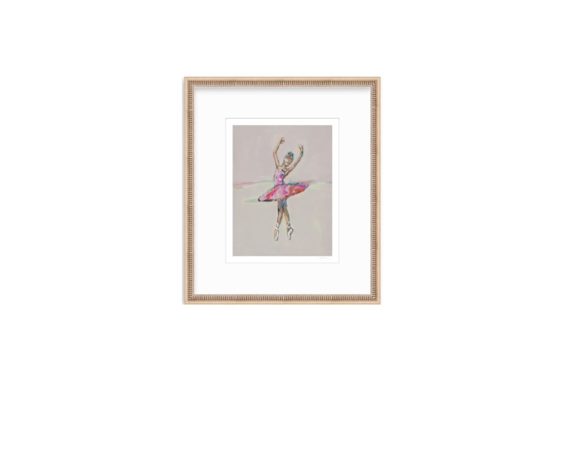 A framed art print featuring a colorful watercolor-style illustration of a ballerina on a light gray background, set in a light wood frame with a white mat.