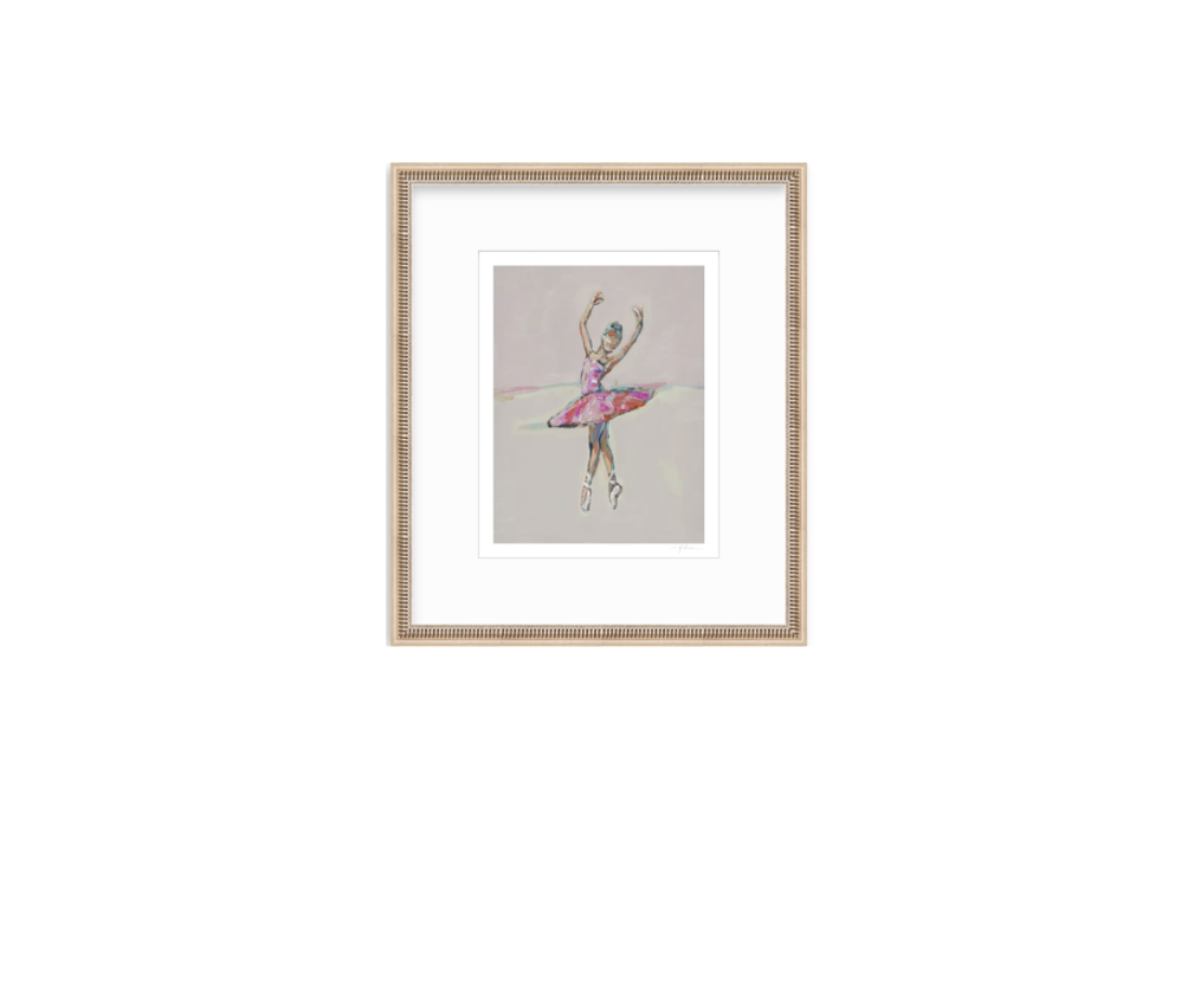 A framed art print featuring a colorful watercolor-style illustration of a ballerina on a light gray background, set in a light wood frame with a white mat.