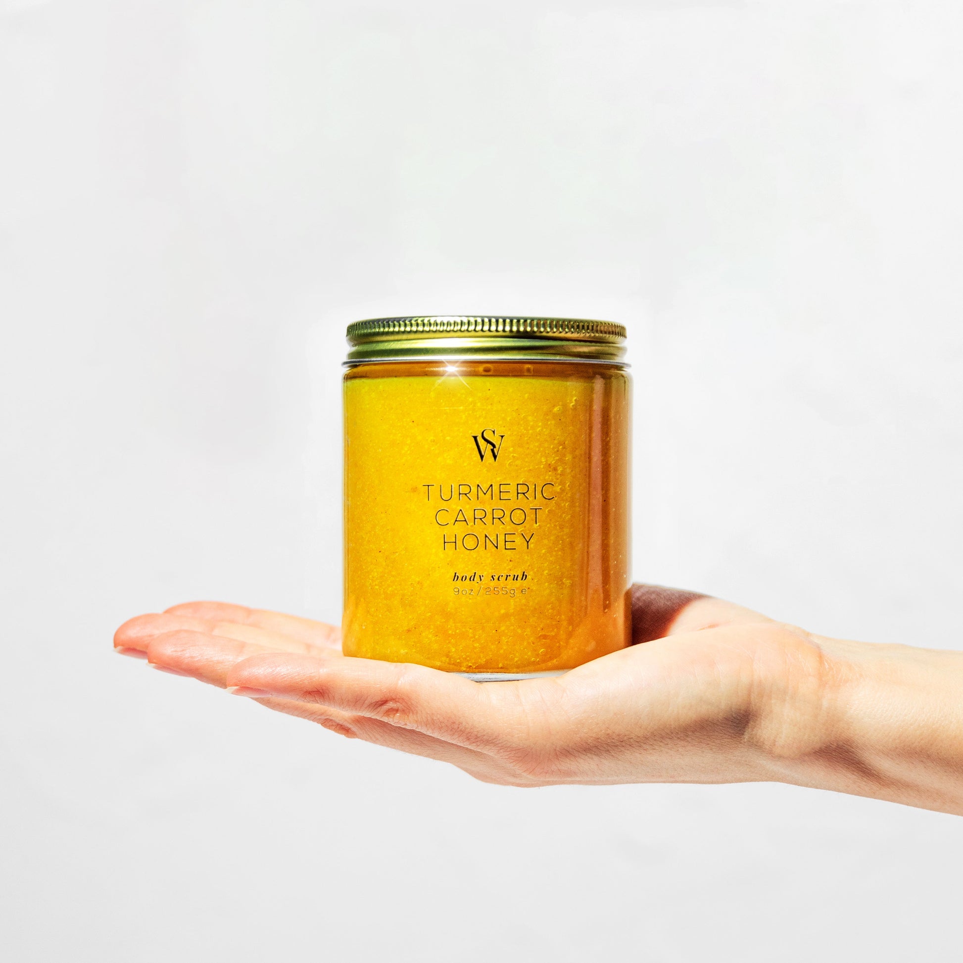 Jar of turmeric carrot honey body scrub held in a hand against a light gray background