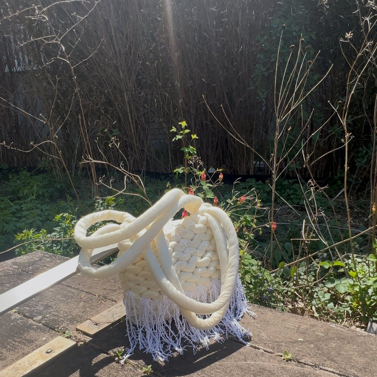 White woven chair with fringe on a stone surface in a garden setting