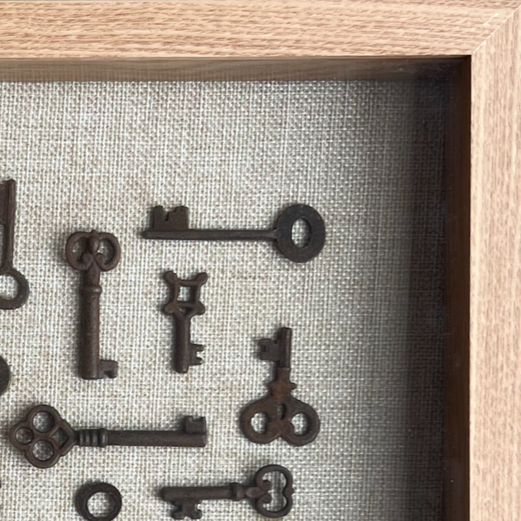 Decorative arrangement of vintage keys on a textured fabric background inside a wooden frame.