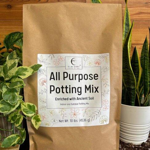 Bag of all-purpose potting mix with a label on a wooden surface surrounded by plants.