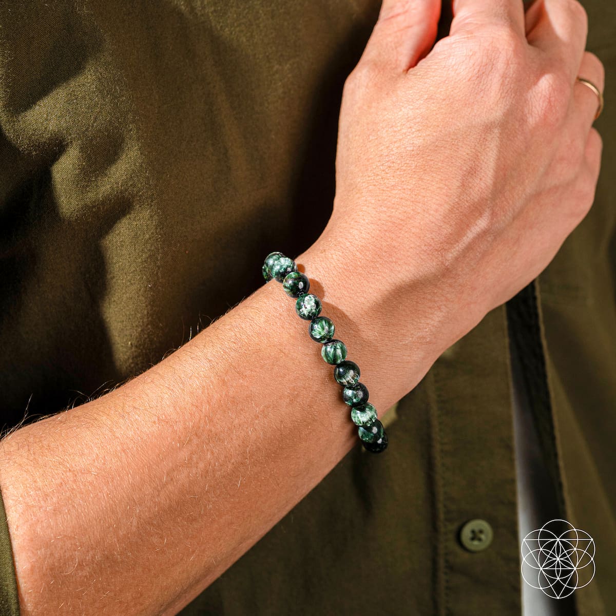 Hand wearing a green beaded bracelet on a brown background
