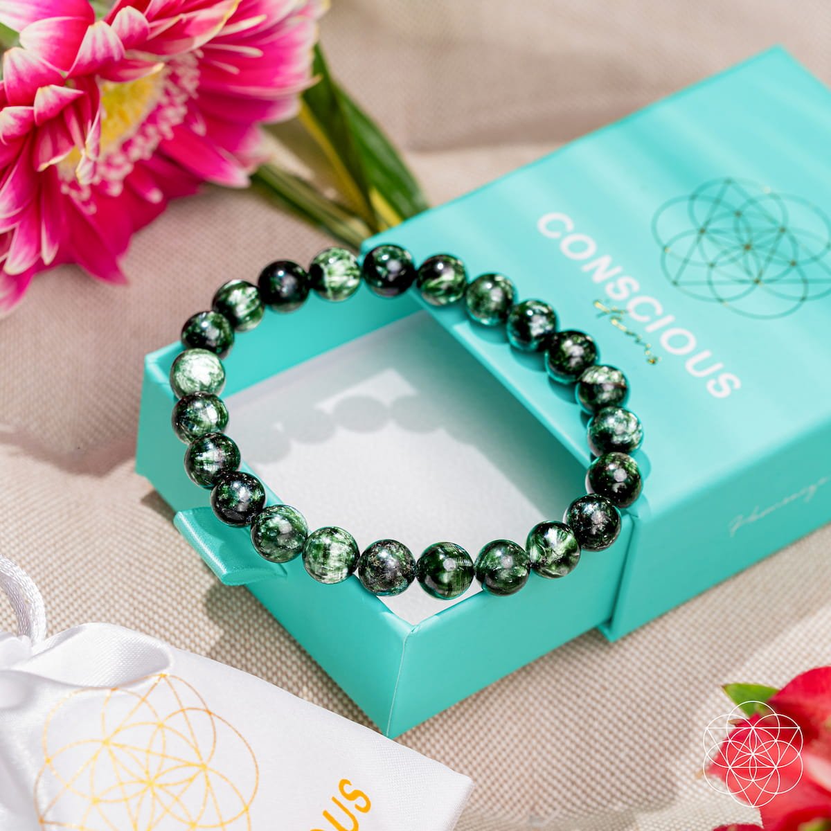 Green beaded bracelet on a turquoise box with pink flowers in the background