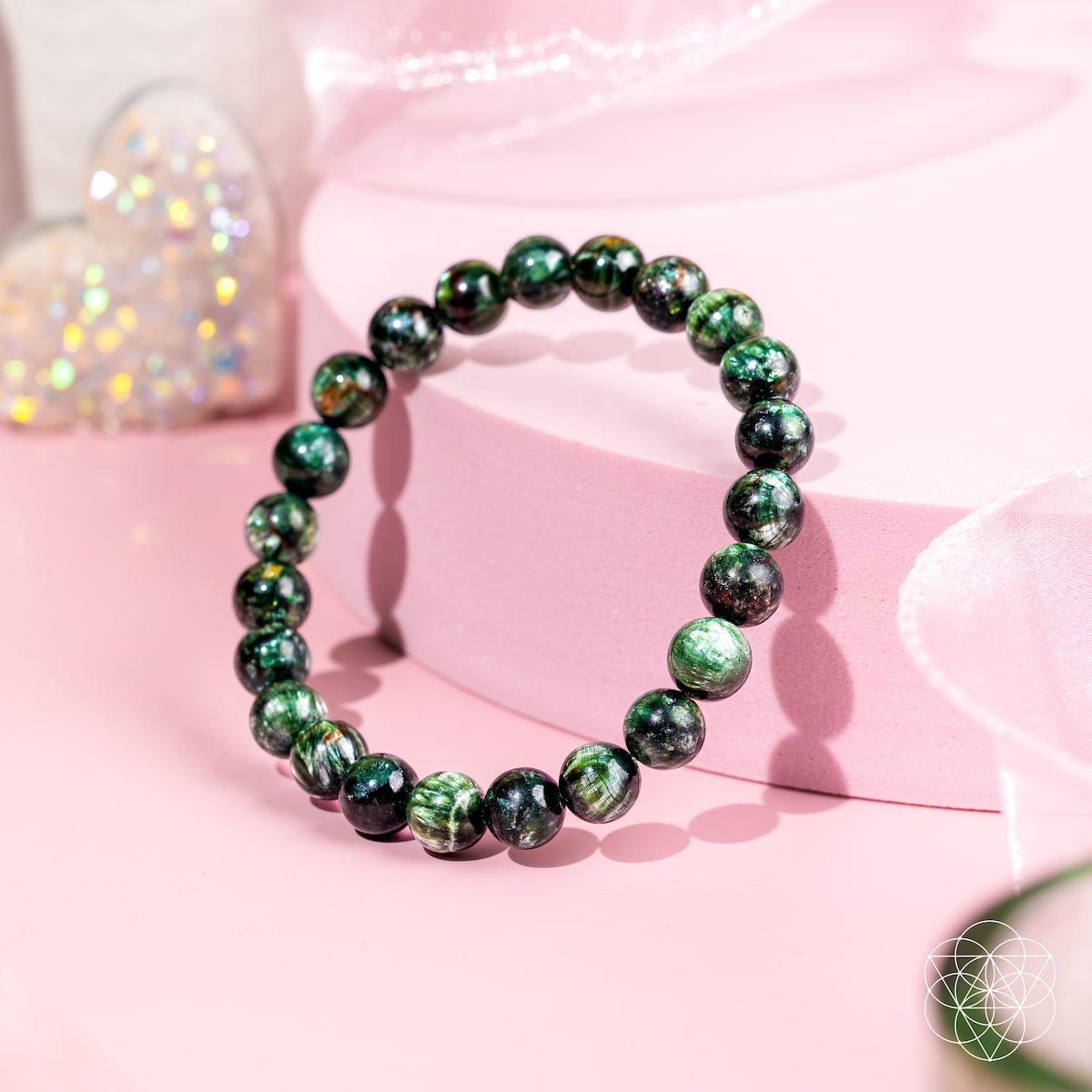 Green beaded bracelet on a pink surface with a blurred decorative object in the background