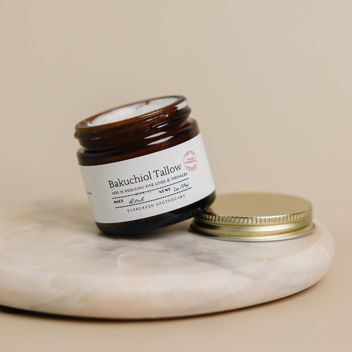 Jar of Bakuchiol Tallow on a marble surface with a beige background