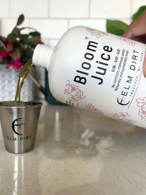 Bottle of 'Bloom Juice' being poured into a metal cup on a kitchen counter.